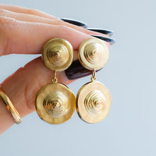 Load image into Gallery viewer, Gold spiral earrings held by a hand against a light blue background