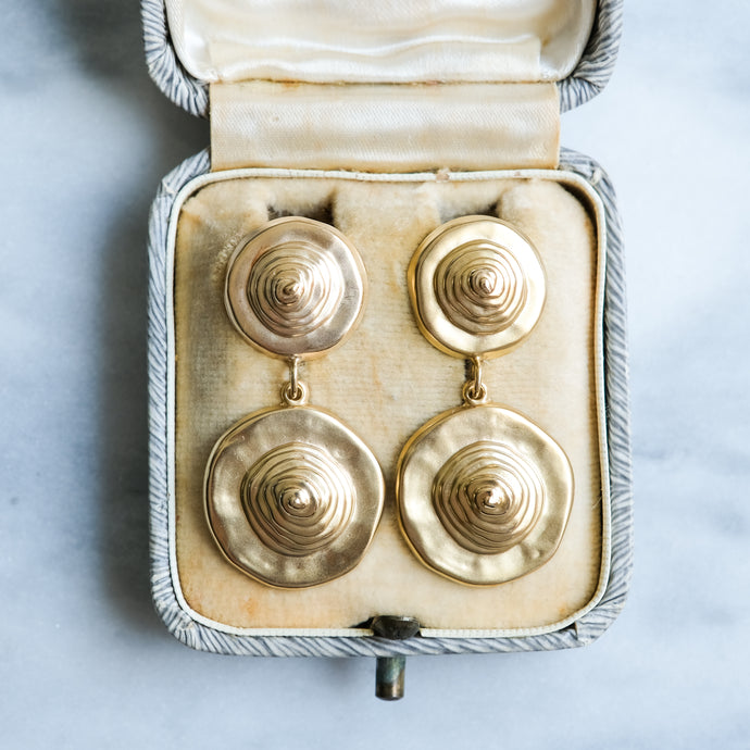 Pair of gold earrings in an open jewelry box on a light blue background